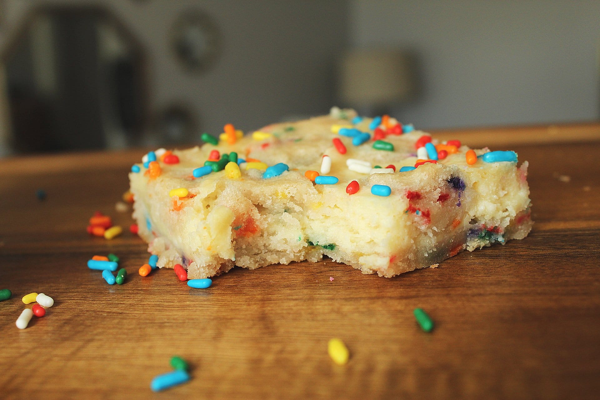 Close-up of a funfetti cheesecake bar with vibrant rainbow sprinkles on a wooden surface, epitomizing the festive spirit of funfetti cheesecake bars.