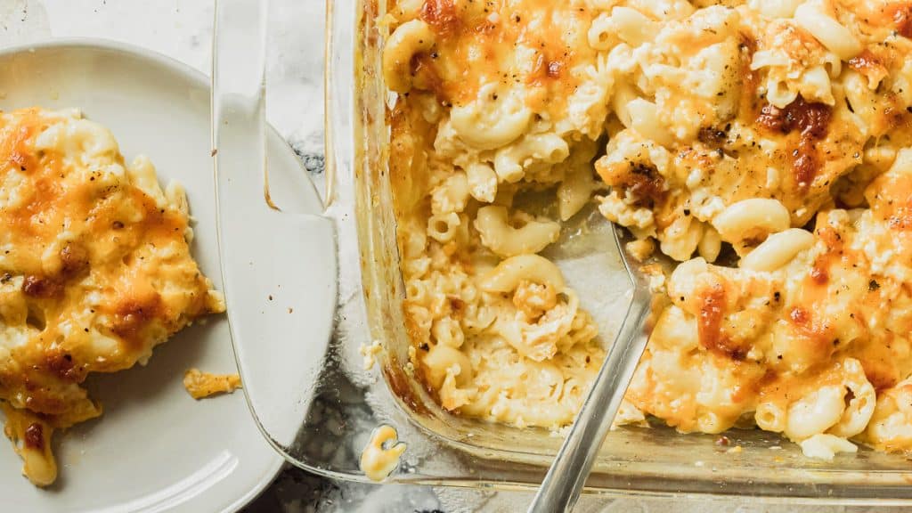 overhead view of a pan of mac and cheese with a spoon, and a small plate with a portion of mac and cheese on it