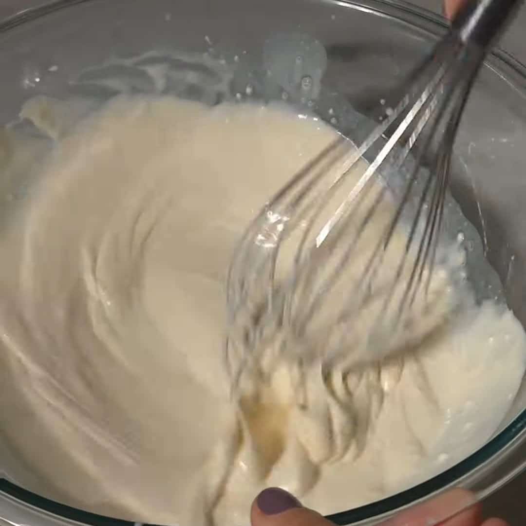 Whisking milk with mascarpone in a glass bowl for southern style mac and cheese recipe.