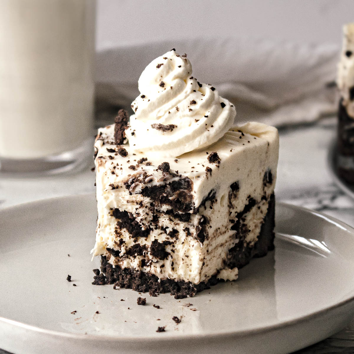 A slice of easy no bake oreo cheesecake on a plate topped with whipped cream, with a bite cut out.