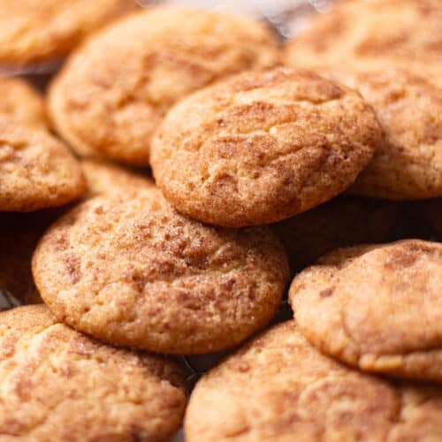 Close-up view of golden brown snickerdoodle cookies with cinnamon sugar tops cooling on a wire rack.