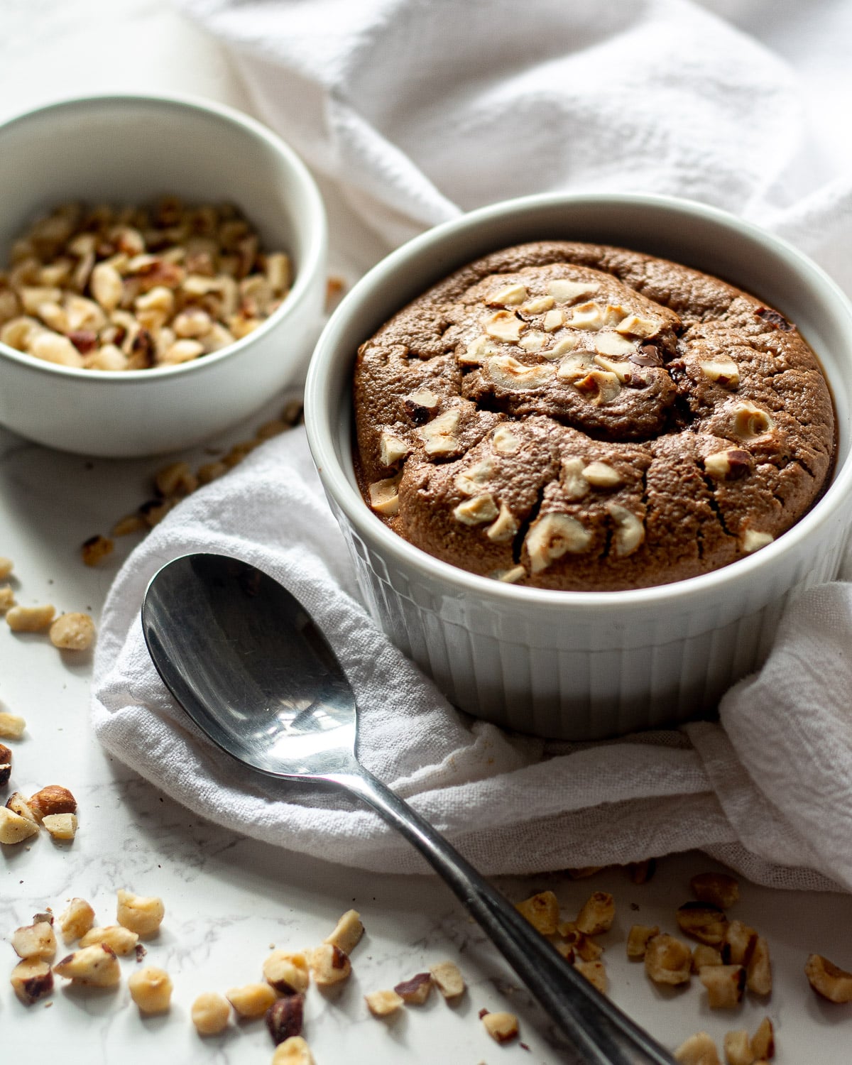 nutella baked oats in the ramekin with hazelnuts in a bowl and scattered around