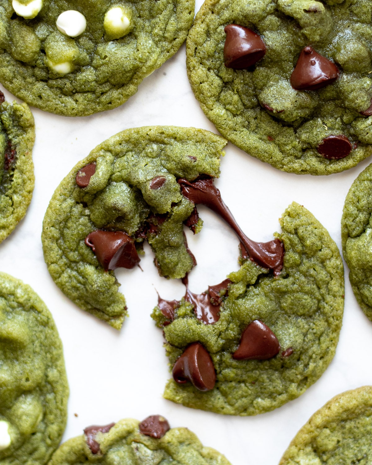 matcha chocolate chip cookies on a tray, one broken in half with melty chocolate chips