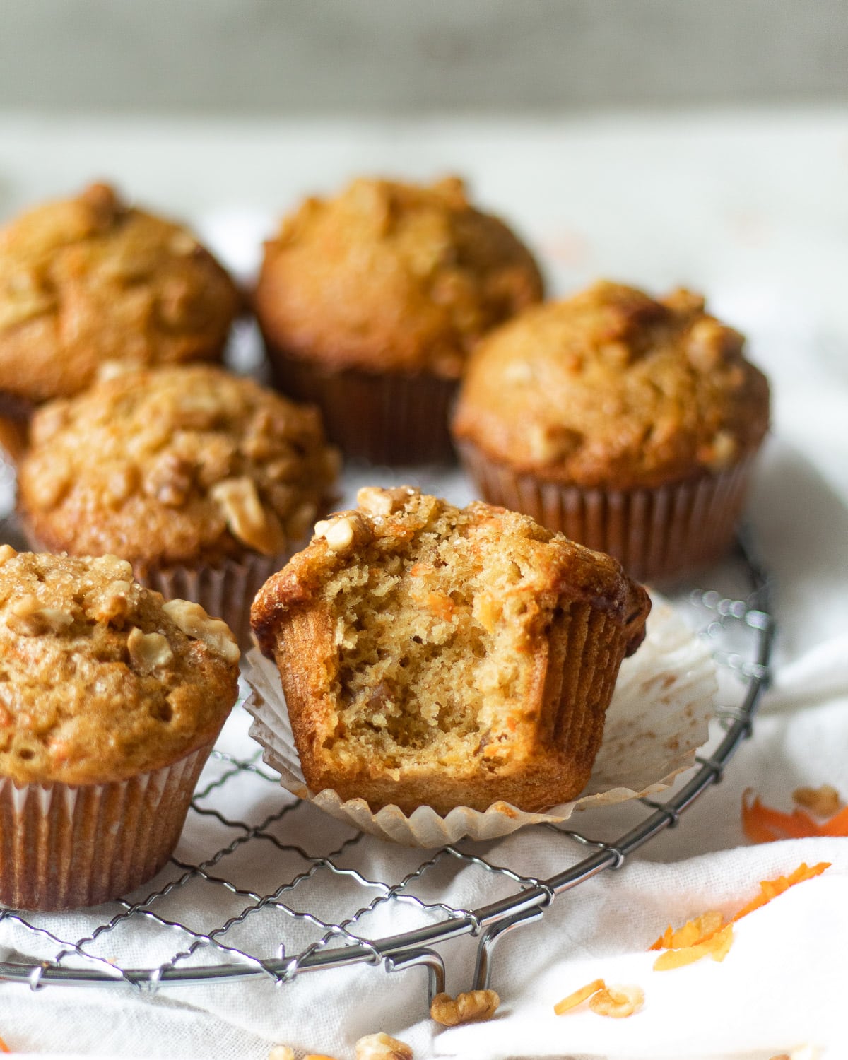 simple banana carrot muffins on a rack, one with a bite taken out