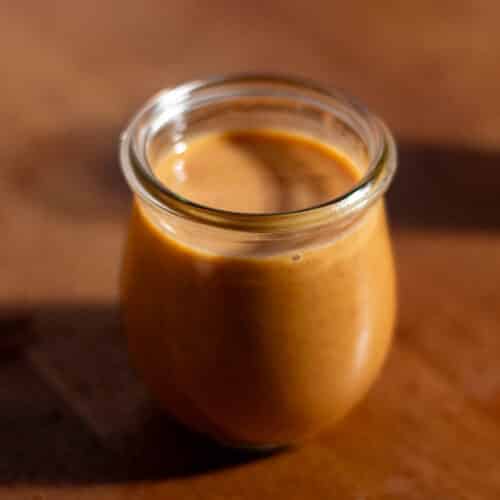 A glass jar filled with copycat Starbucks pumpkin sauce on a wooden counter.