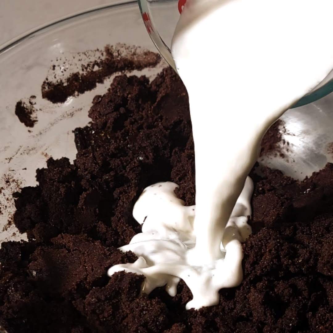 Creamy buttermilk being poured into a bowl of chocolate crumbles to form a luscious batter for Matilda's Chocolate Cake.