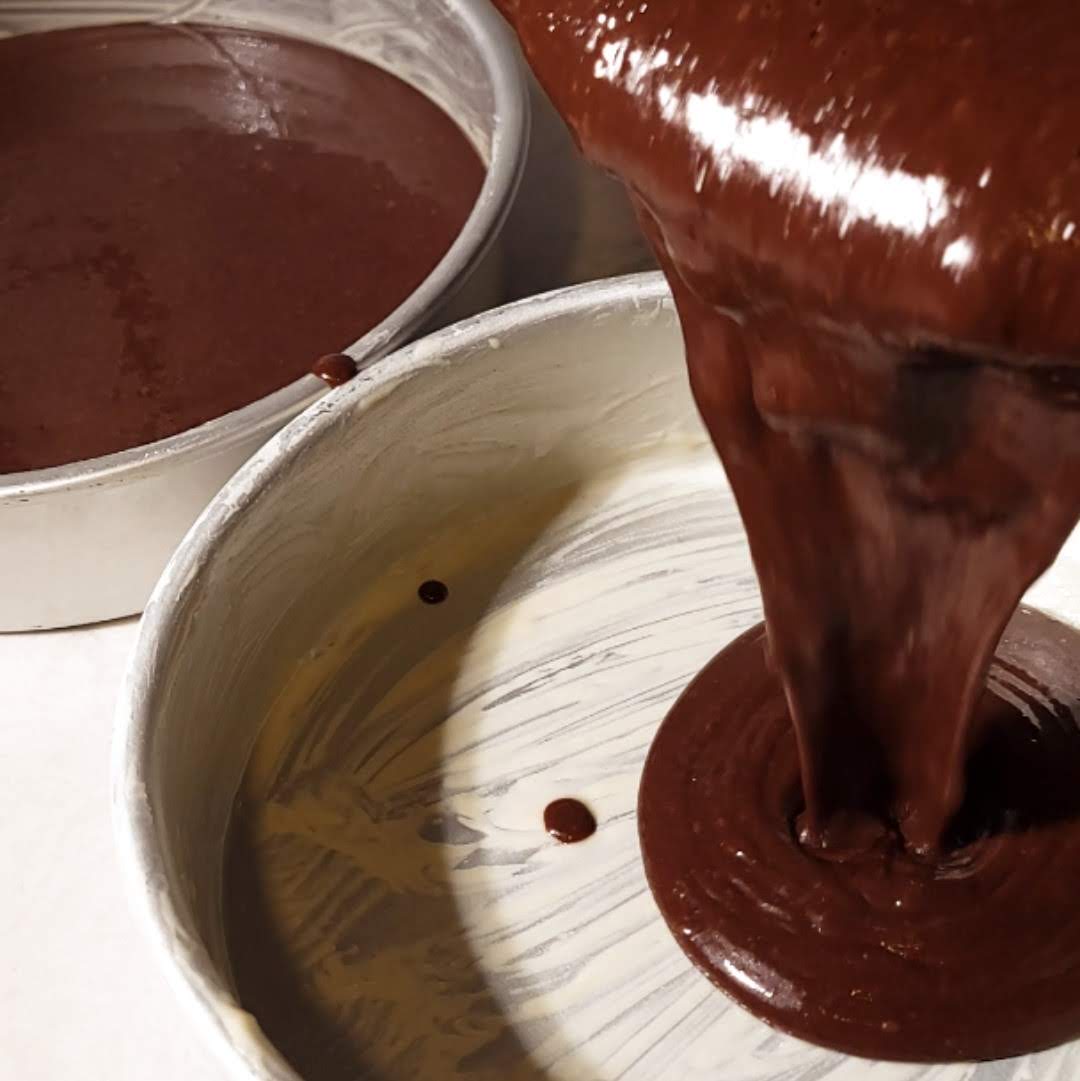 Smooth chocolate cake batter being poured into baking pans, ready for the oven in the process of making Matilda's Chocolate Cake.