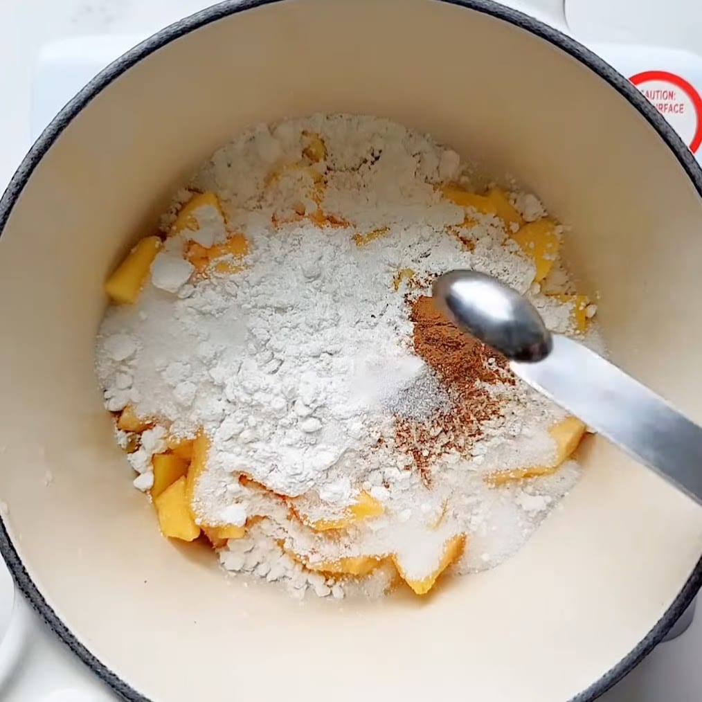 mixing peaches, mangoes, and other ingredients in a saucepan for peach mango pies.