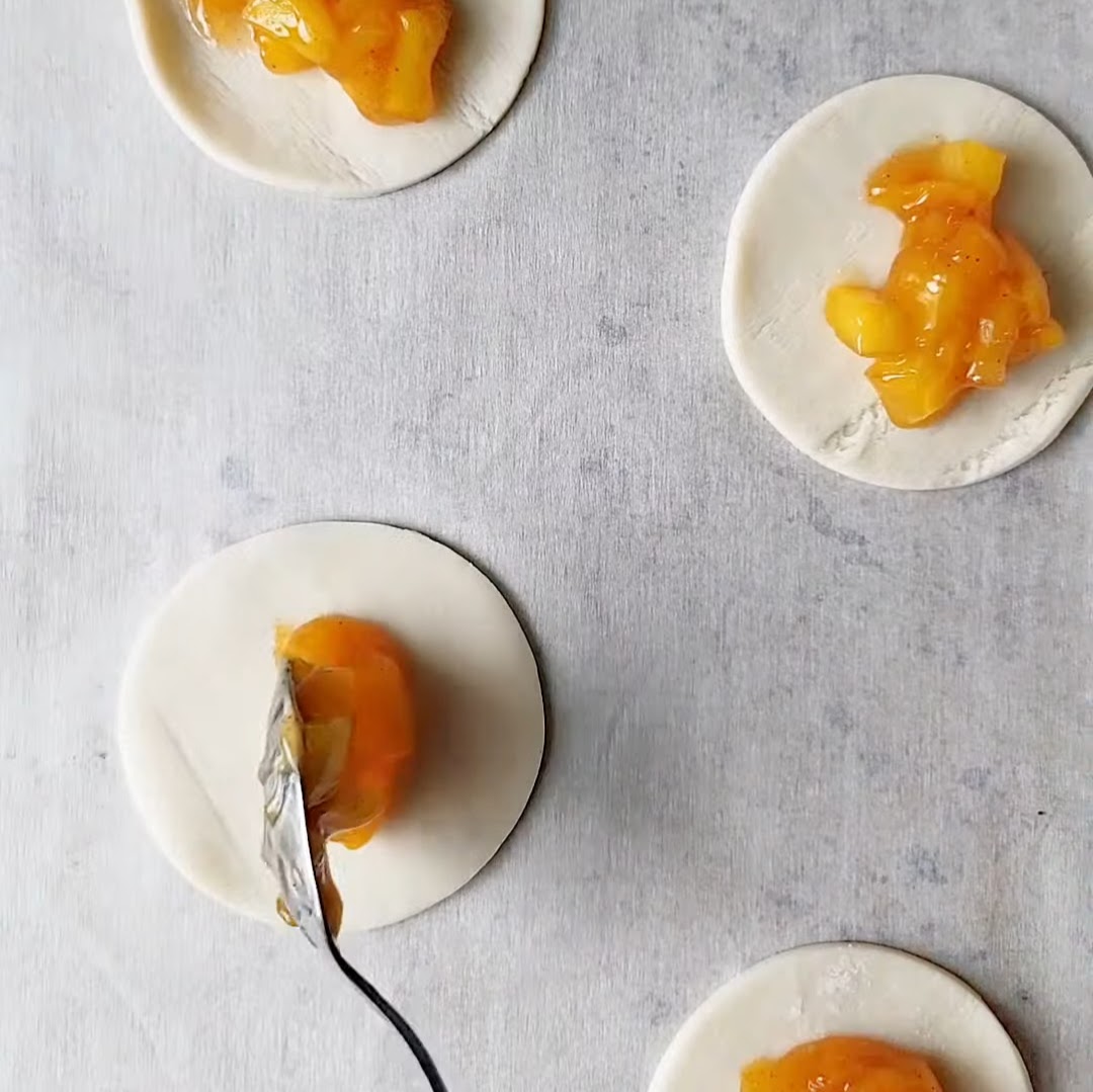 Spooning peach mango pie filling into pie crust.