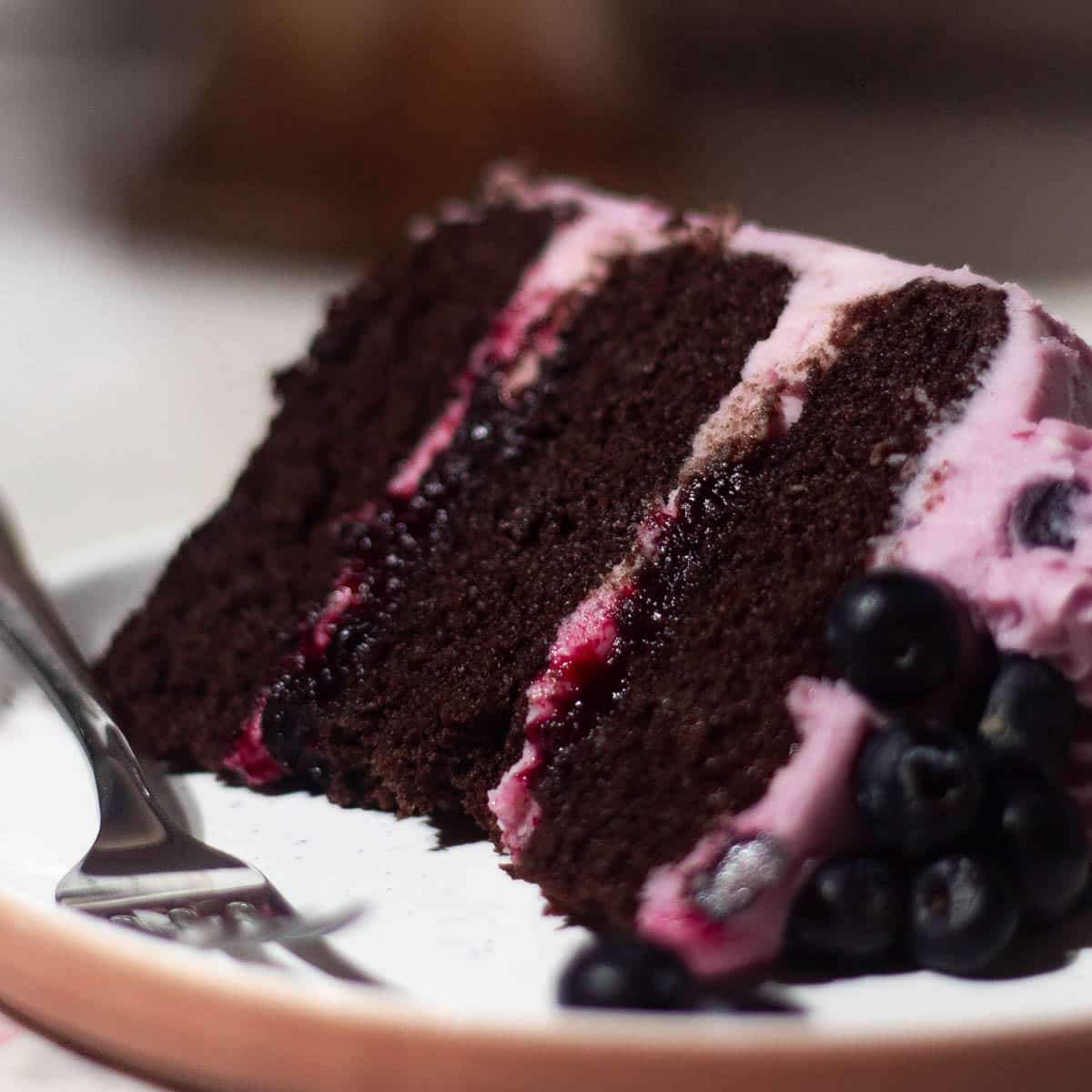 Chocolate blueberry cake with three layers of moist chocolate sponge, filled and frosted with blueberry buttercream and topped with fresh blueberries.