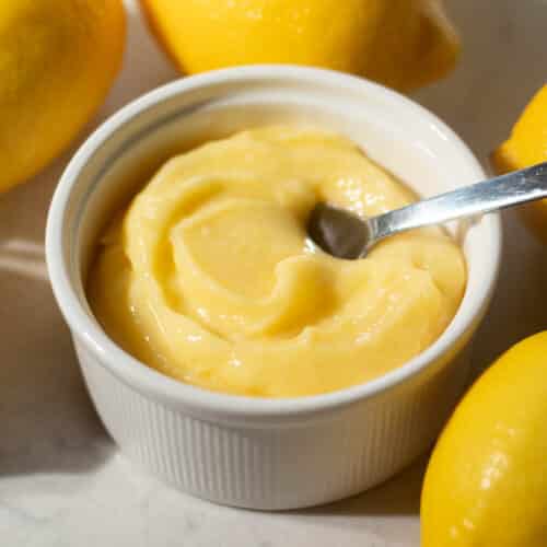 Creamy and smooth simple lemon curd swirled in a white ramekin, surrounded by fresh lemons.