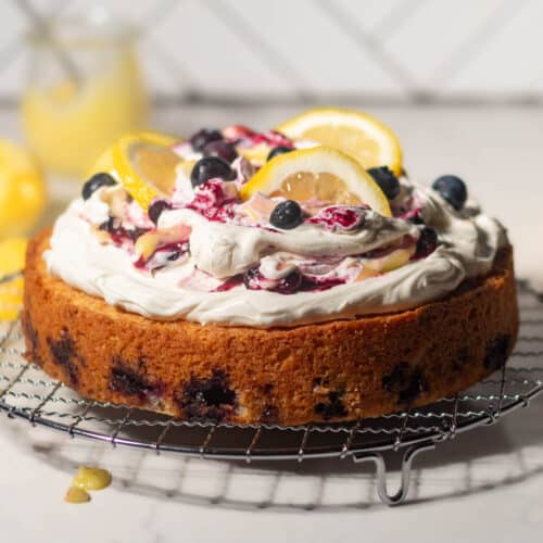 Full lemon blueberry mascarpone cake presented on a metal rack, topped with swirled mascarpone cream, blueberries, and lemon slices for a fresh and vibrant finish.