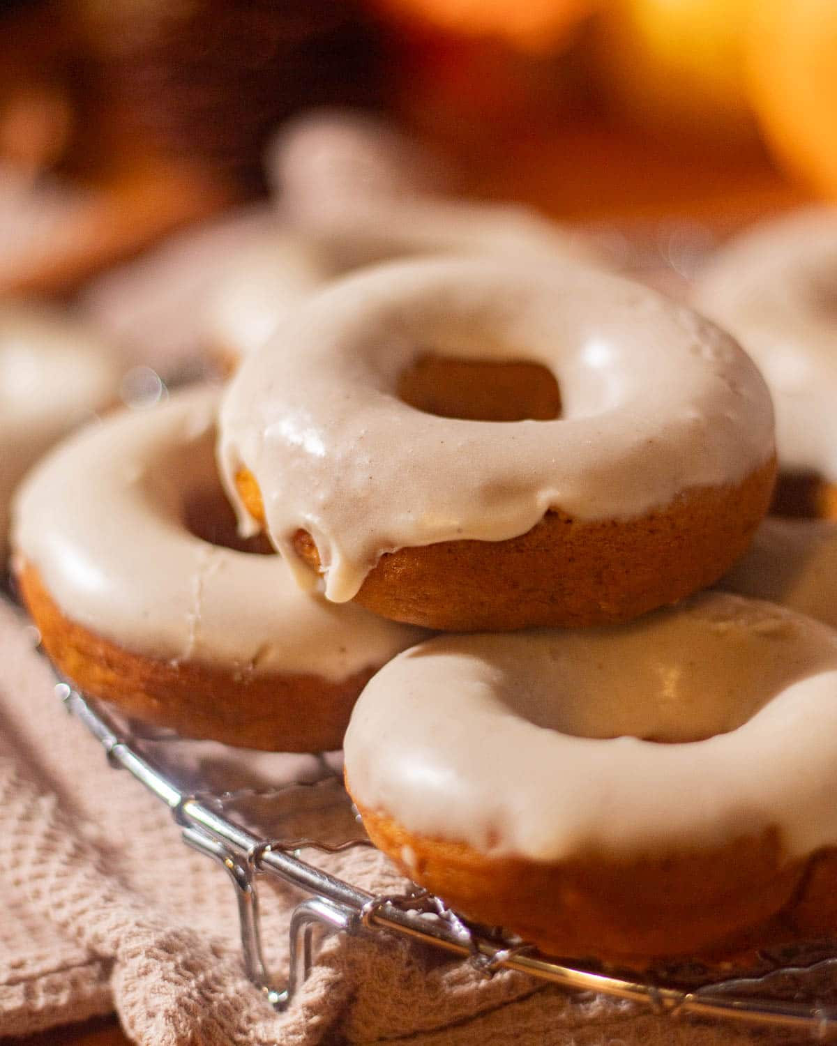 A cooling rack filled with warm pumpkin spice donuts, each covered in a thick layer of drippy brown butter glaze, photographed in natural light.