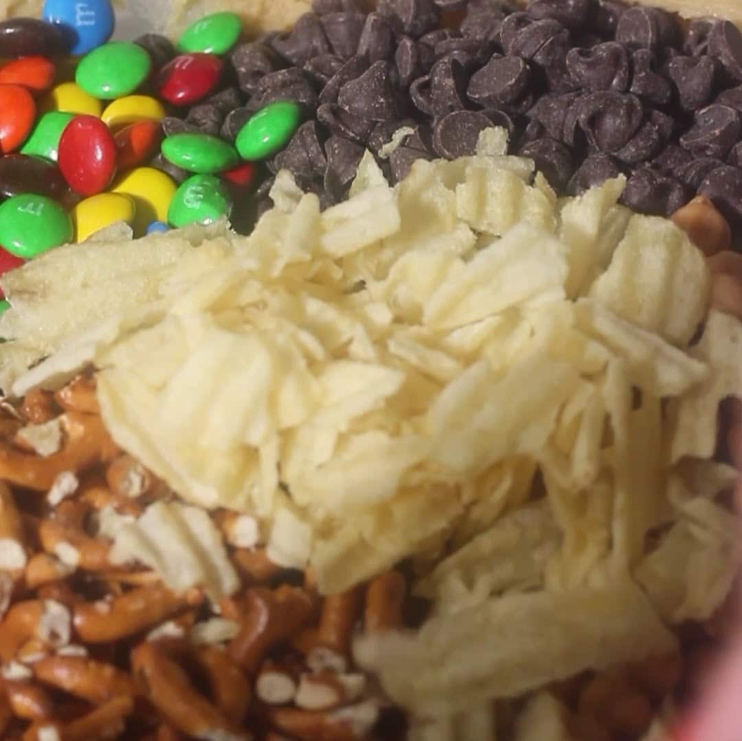 Bowl filled with colorful M&Ms, chocolate chips, pretzels, and potato chips for kitchen sink cookie mix-ins.