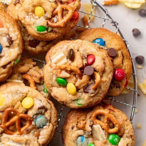 Stack of golden brown kitchen sink cookies packed with pretzels, potato chips, and candy pieces for the ultimate everything-but-the-kitchen-sink dessert.