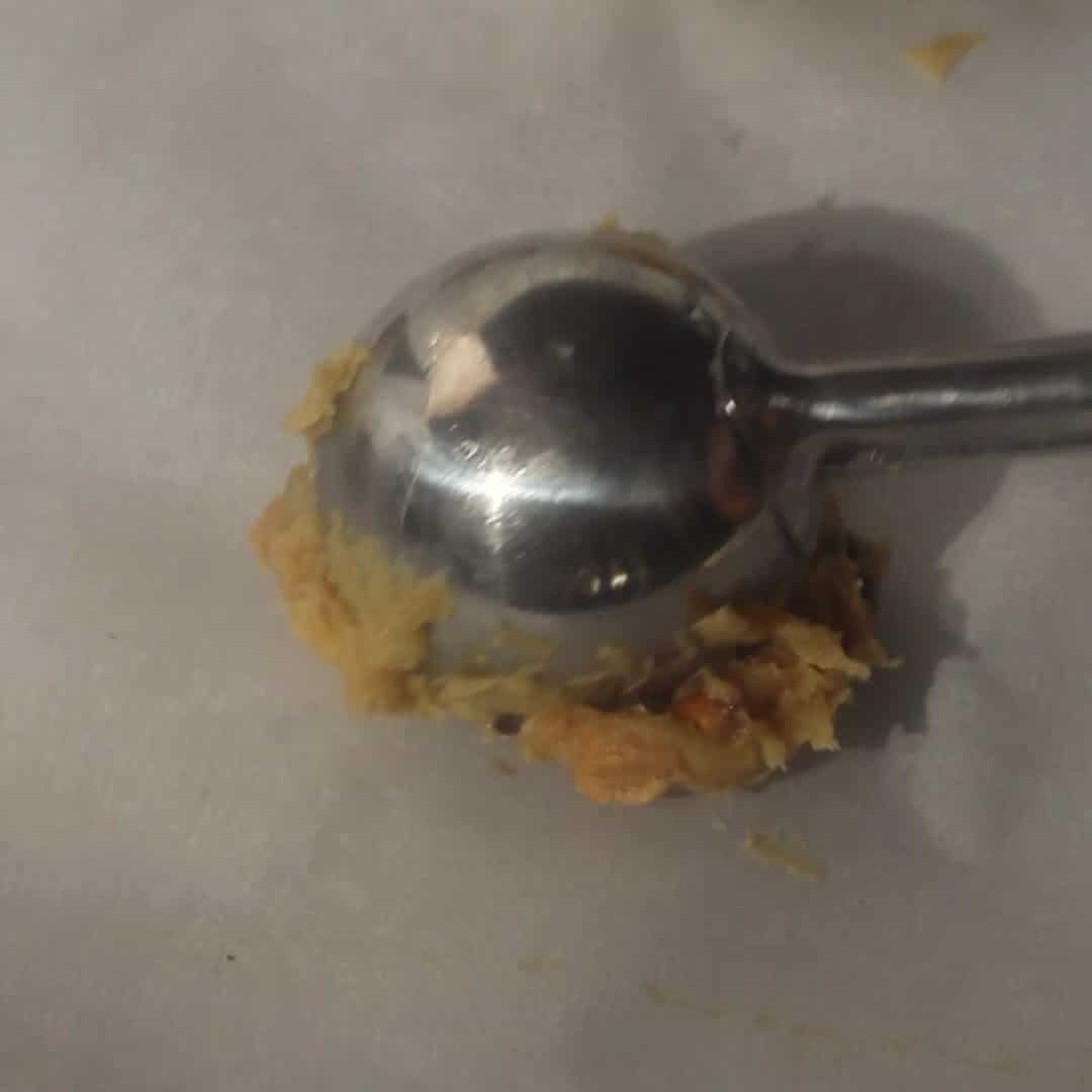 Cookie scoop dropping chewy kitchen sink cookie dough onto a parchment-lined baking sheet.