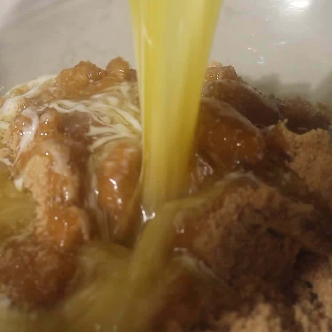 Stream of melted butter poured over packed brown sugar to begin kitchen sink cookie dough.