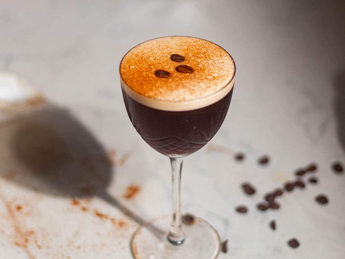 Elegant rum espresso martini in a coupe glass with coffee beans scattered around on the table.