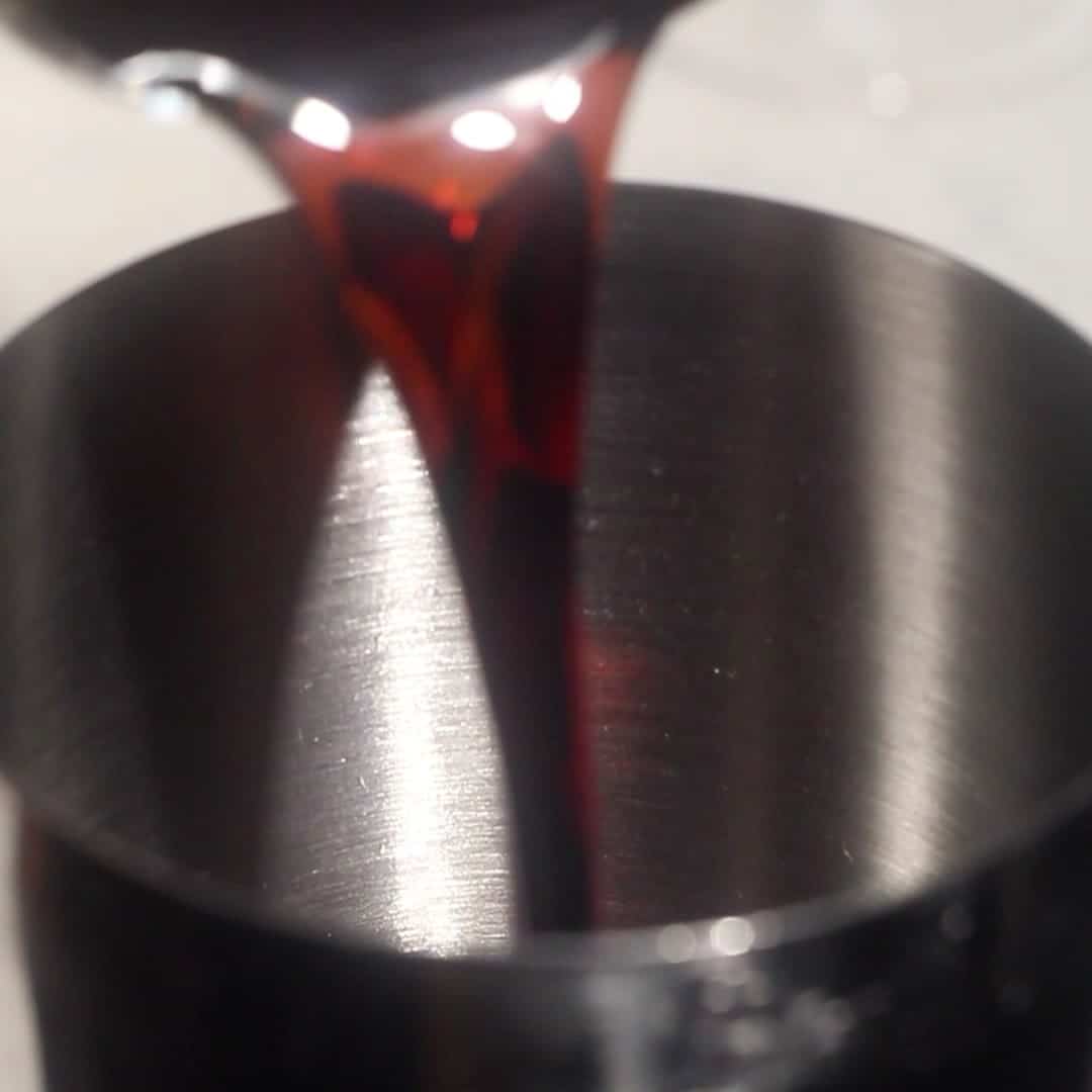 Pouring dark rum into a cocktail shaker to make a spiced rum espresso martini.