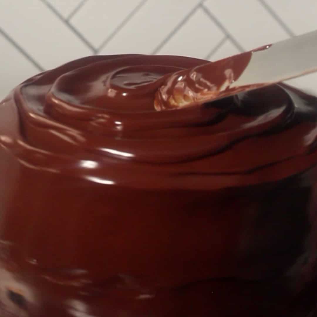 Spreading shiny chocolate ganache over the layered chocolate mousse cake for a smooth finish.