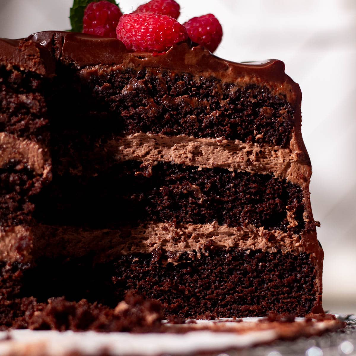 Moist chocolate cake with chocolate mousse filling between layers, topped with thick chocolate ganache and fresh berries.