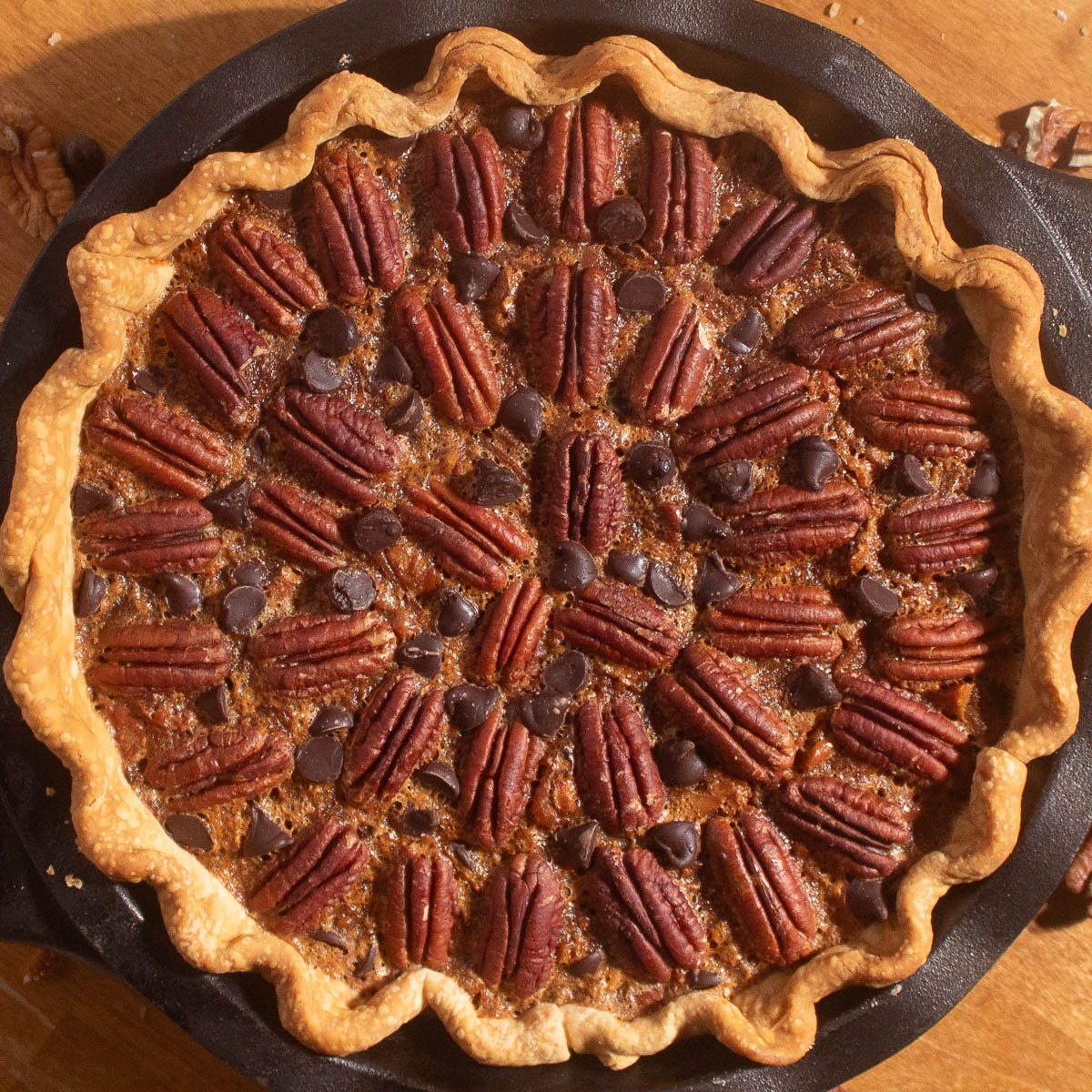 Golden chocolate chip pecan pie recipe baked in a cast iron pan with pecans and chocolate chips on top.