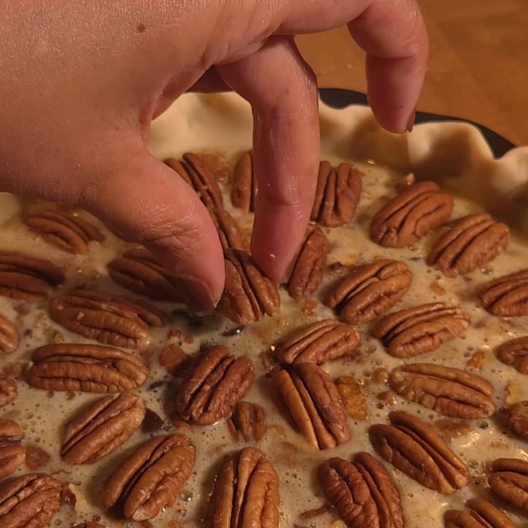 Unbaked chocolate chip pecan pie with pecans and chocolate chips arranged over brown sugar filling before baking.