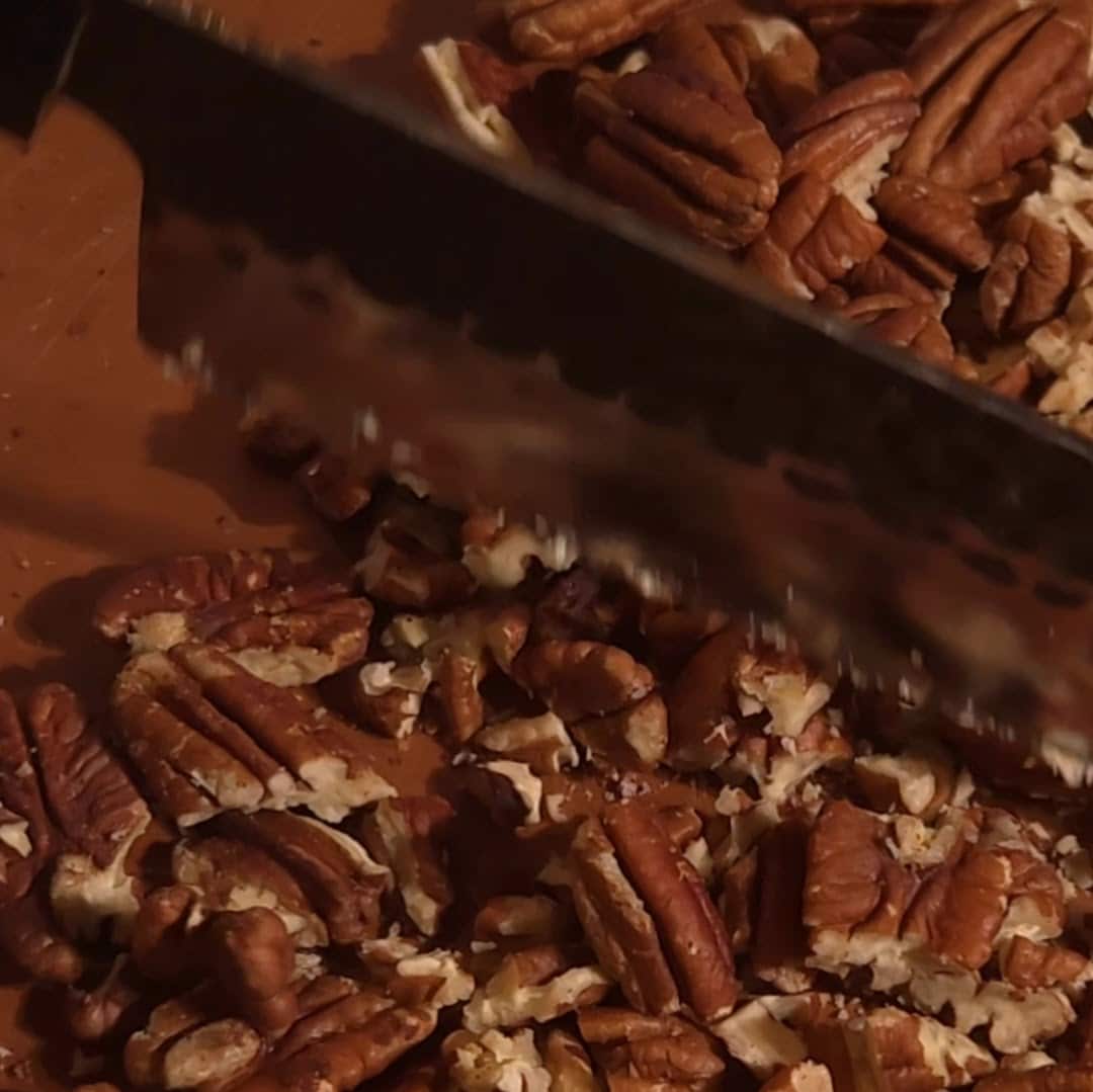 Chopping pecans on a wooden cutting board for the pecan pie filling.