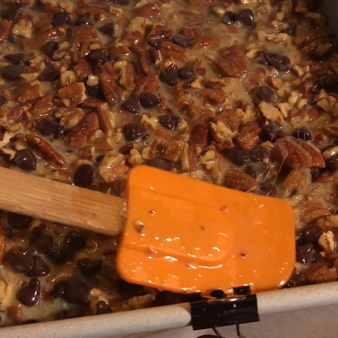 Spreading chocolate pecan filling evenly in a baking pan before baking.