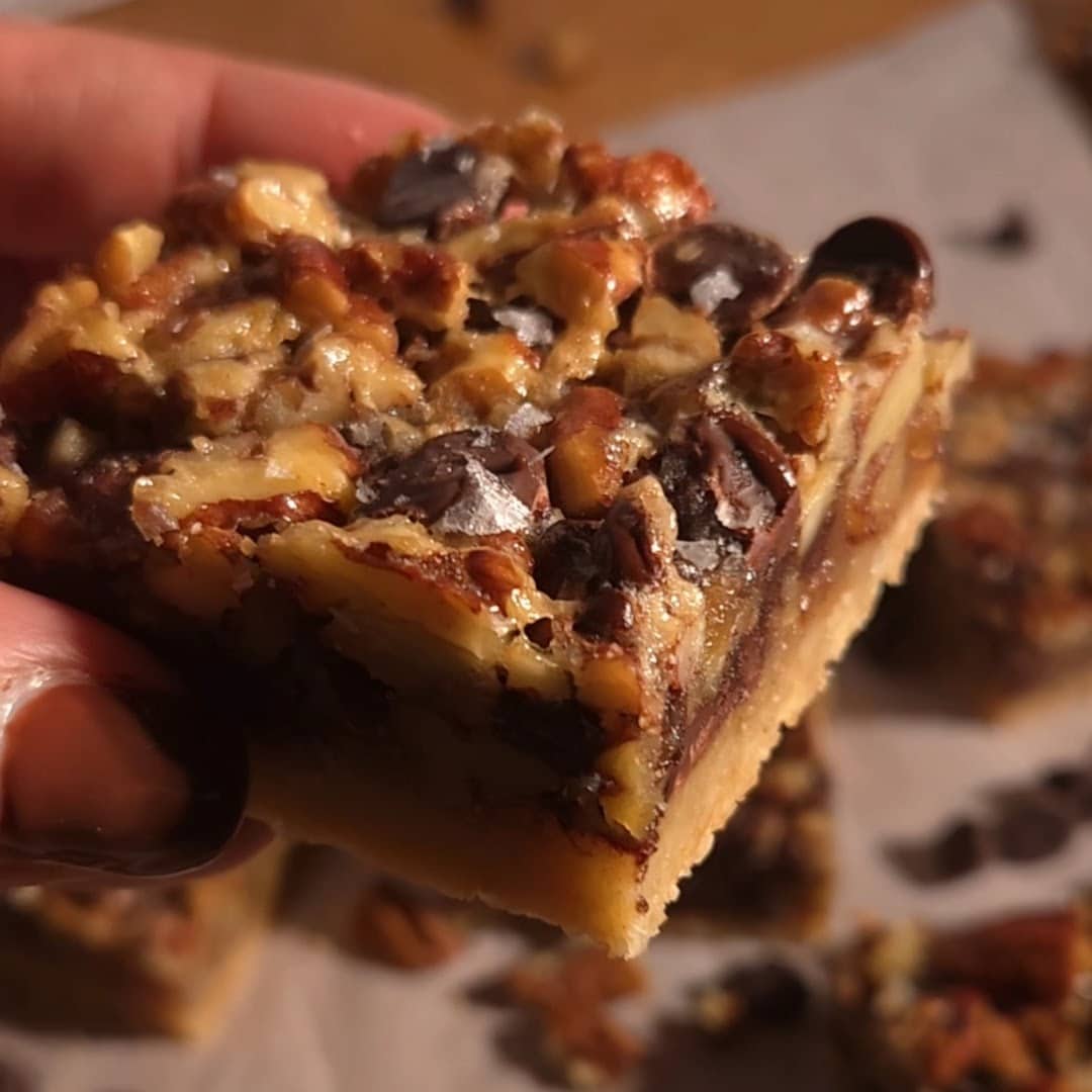 Gooey square of chocolate pecan pie bar with thick filling and a golden crust.