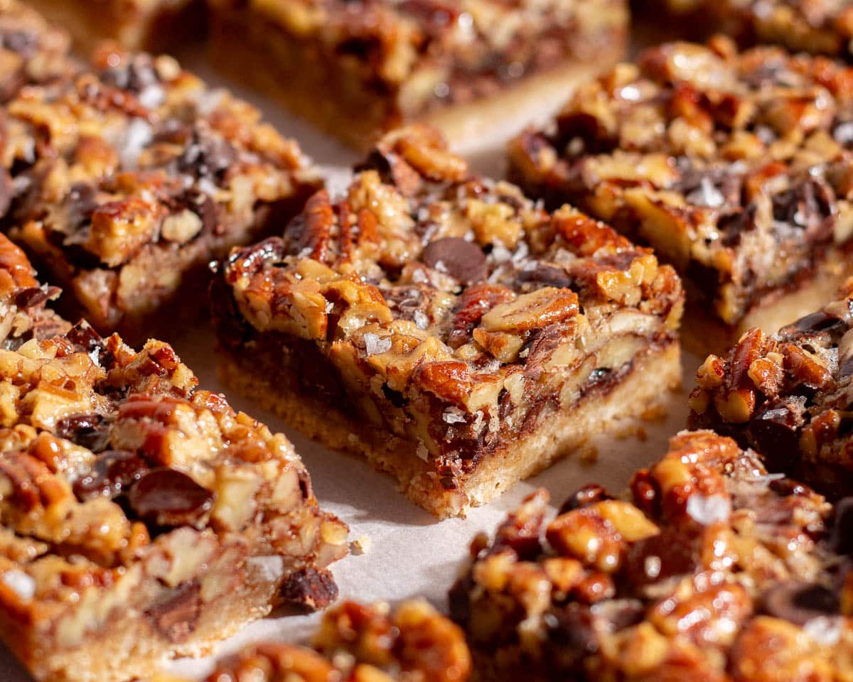 Close-up of baked chocolate pecan pie bars with layers of chocolate chips, toasted pecans, and golden shortbread crust.