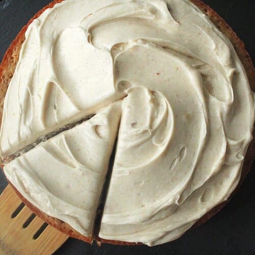 Browned butter cream cheese frosting spread on a round cake with smooth swirls and a slice removed showing creamy brown butter frosting texture.