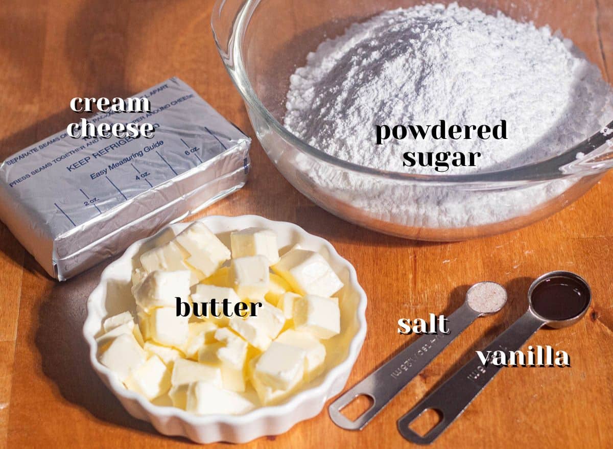 Measured ingredients for browned butter cream cheese frosting including butter cubes, powdered sugar, cream cheese, vanilla extract, and salt.