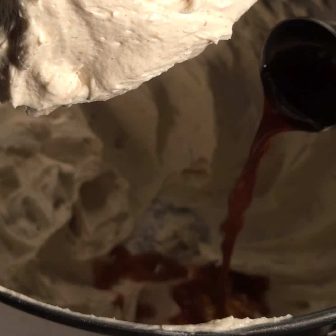 Brown butter being poured into cream cheese mixture in a mixing bowl to make browned butter cream cheese frosting.