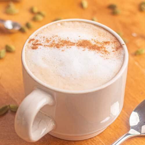 Homemade cardamom latte with creamy milk foam and cardamom spice in a white coffee mug.